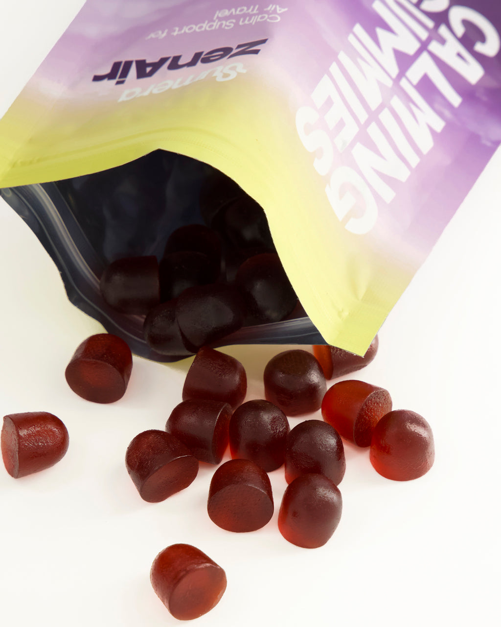 An open Sumera ZenAir pouch tipped on its side on a white surface, with deep red calming gummies spilling out and scattered in front of it.