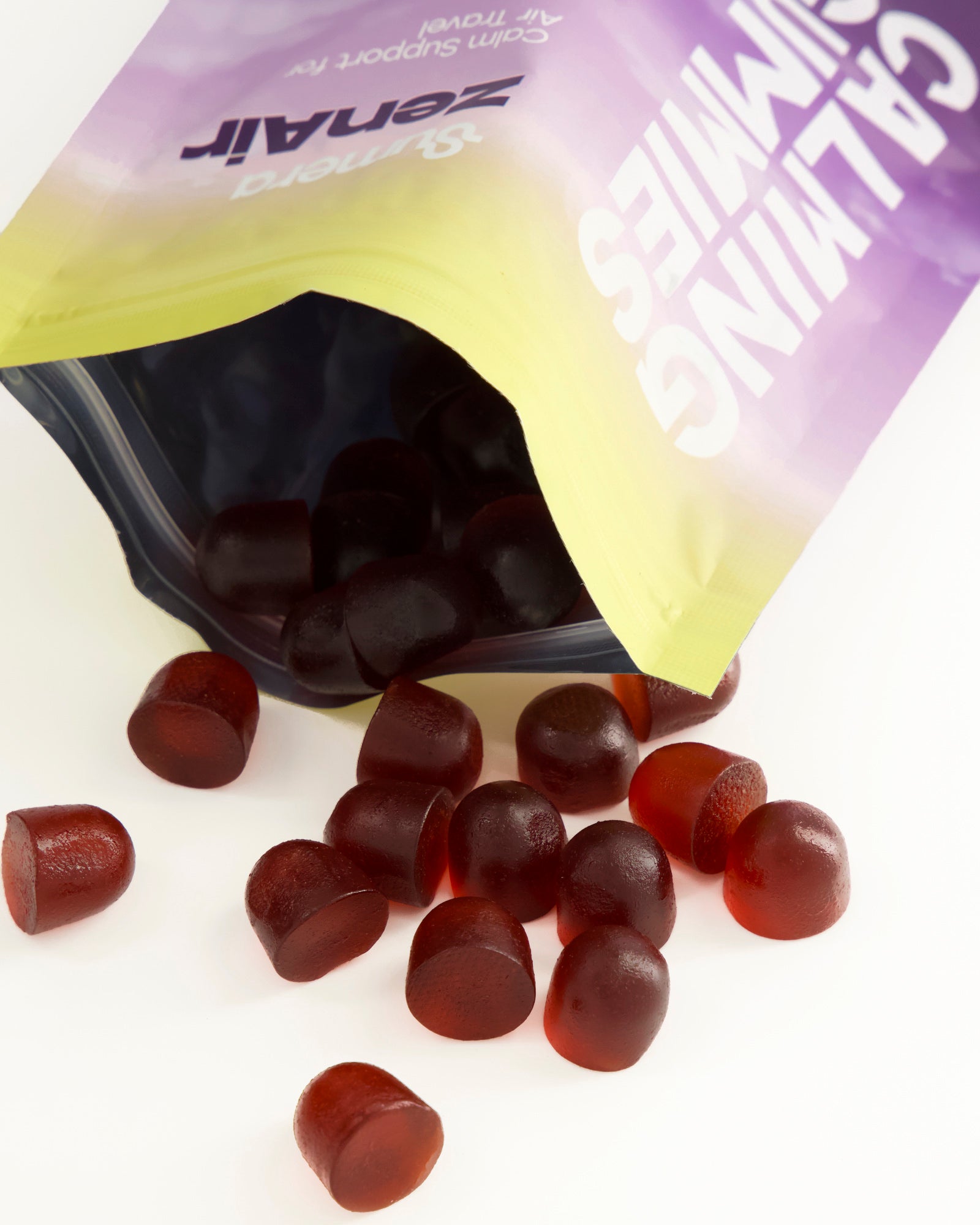 An open Sumera ZenAir pouch tipped on its side on a white surface, with deep red calming gummies spilling out and scattered in front of it.